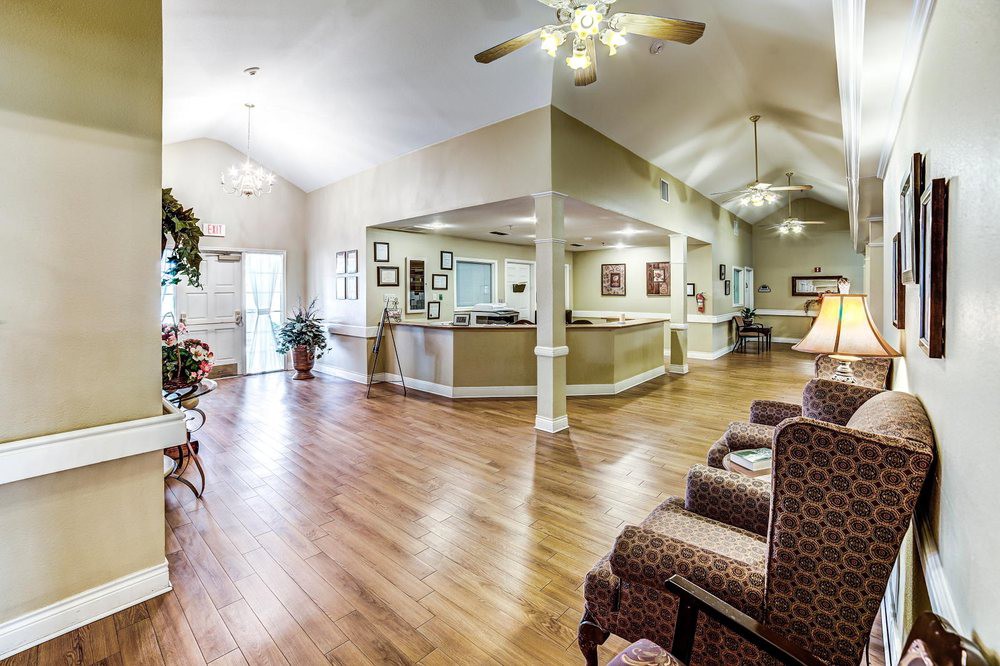 A spacious and well-lit lobby with wooden flooring, seating arrangements, and a reception desk.