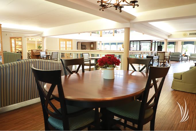 A cozy dining area with a round wooden table surrounded by chairs, featuring a central flower arrangement.