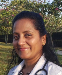 A woman smiling outdoors with trees in the background.