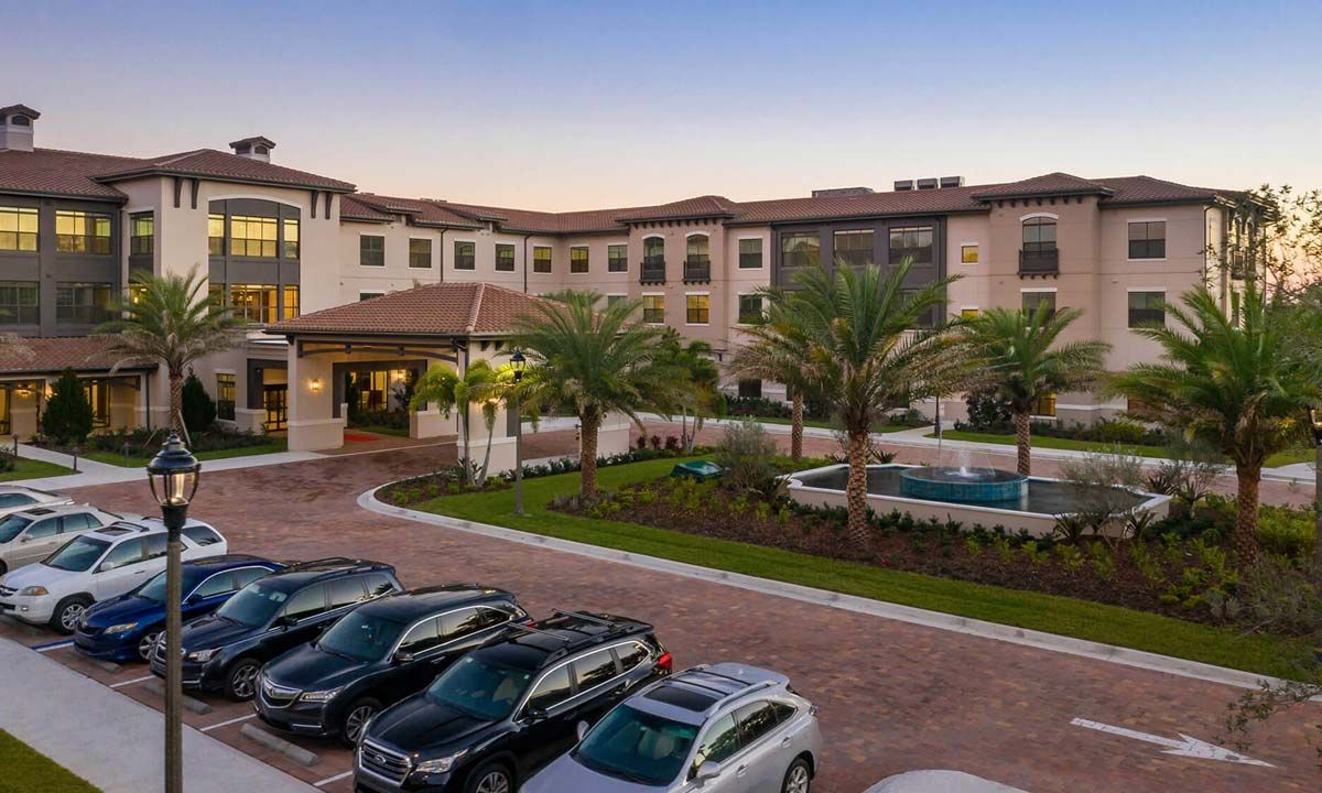 A view of an apartment complex with parked cars and palm trees at sunset.