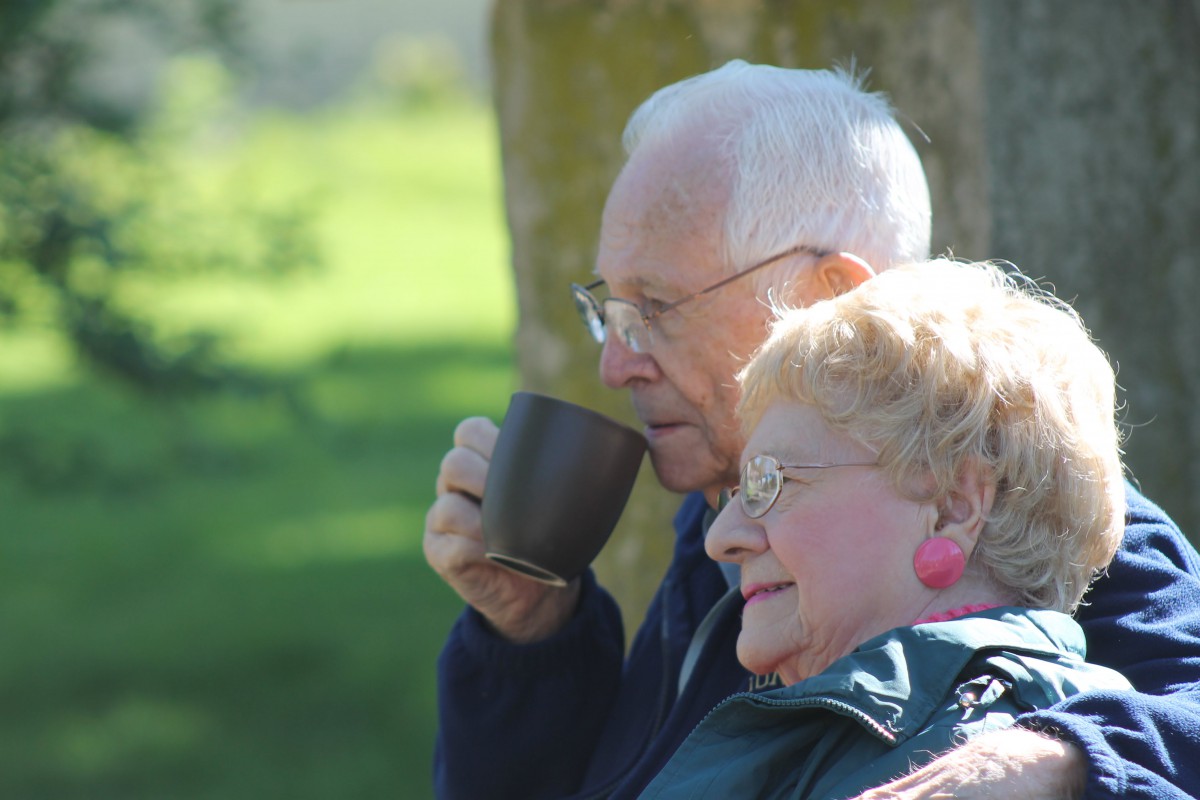 An elderly couple enjoys a peaceful moment outdoors, sipping coffee and embracing nature.