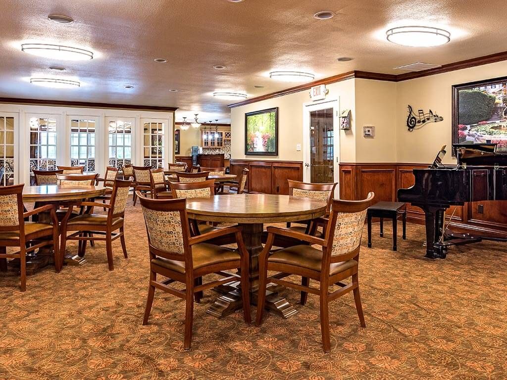 A cozy dining area featuring wooden tables and chairs, with a piano and warm lighting.