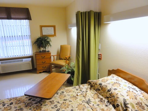 A cozy hospital room with a patient bed, side table, and a green privacy curtain.
