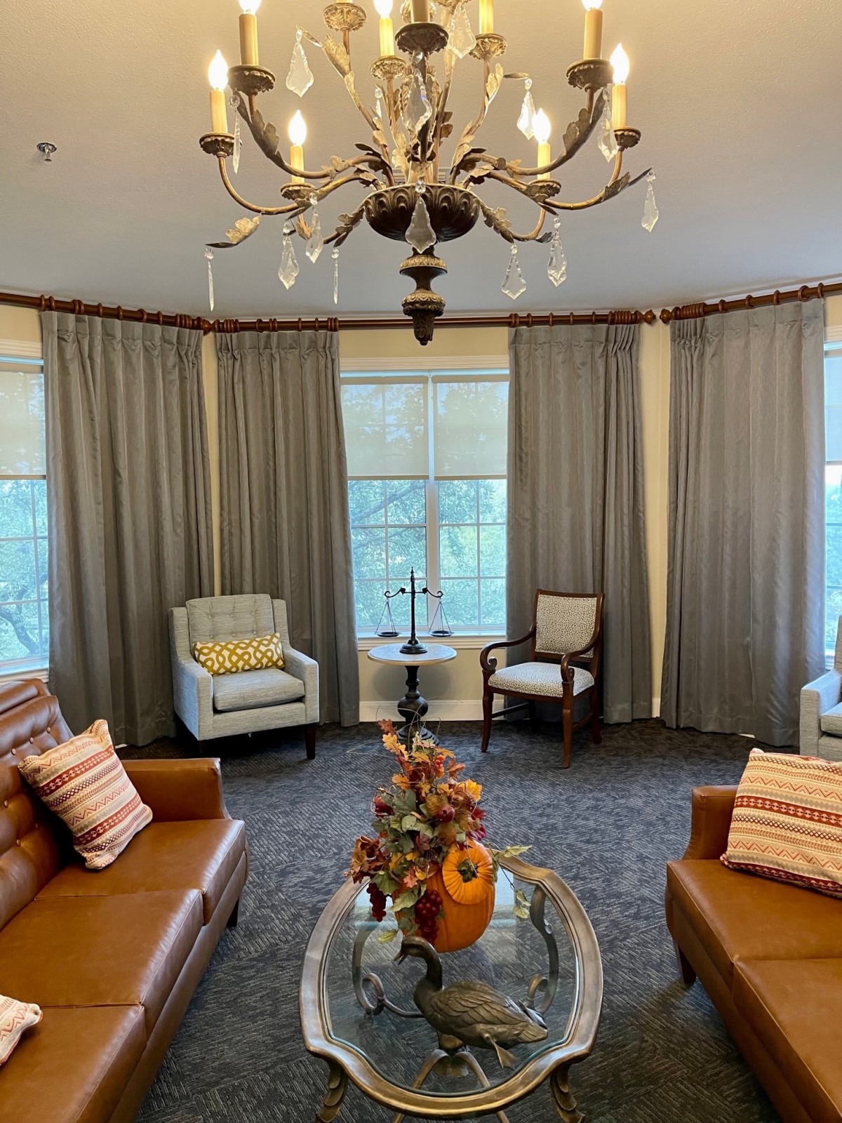 A cozy living room with leather sofas, armchairs, and a decorative coffee table under a chandelier.