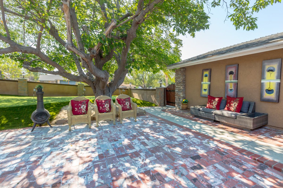A cozy backyard patio with outdoor seating under the shade of a large tree.