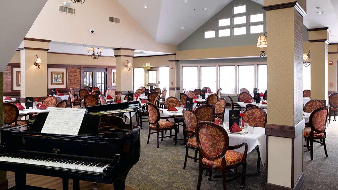 An elegant restaurant dining area featuring a grand piano and neatly arranged tables with upholstered chairs.