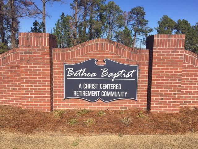 A sign for Bethea Baptist, a Christ-centered retirement community, set against a backdrop of trees.