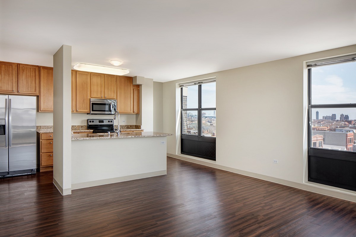 A modern apartment with an open floor plan featuring a kitchen and living area with hardwood floors and large windows.