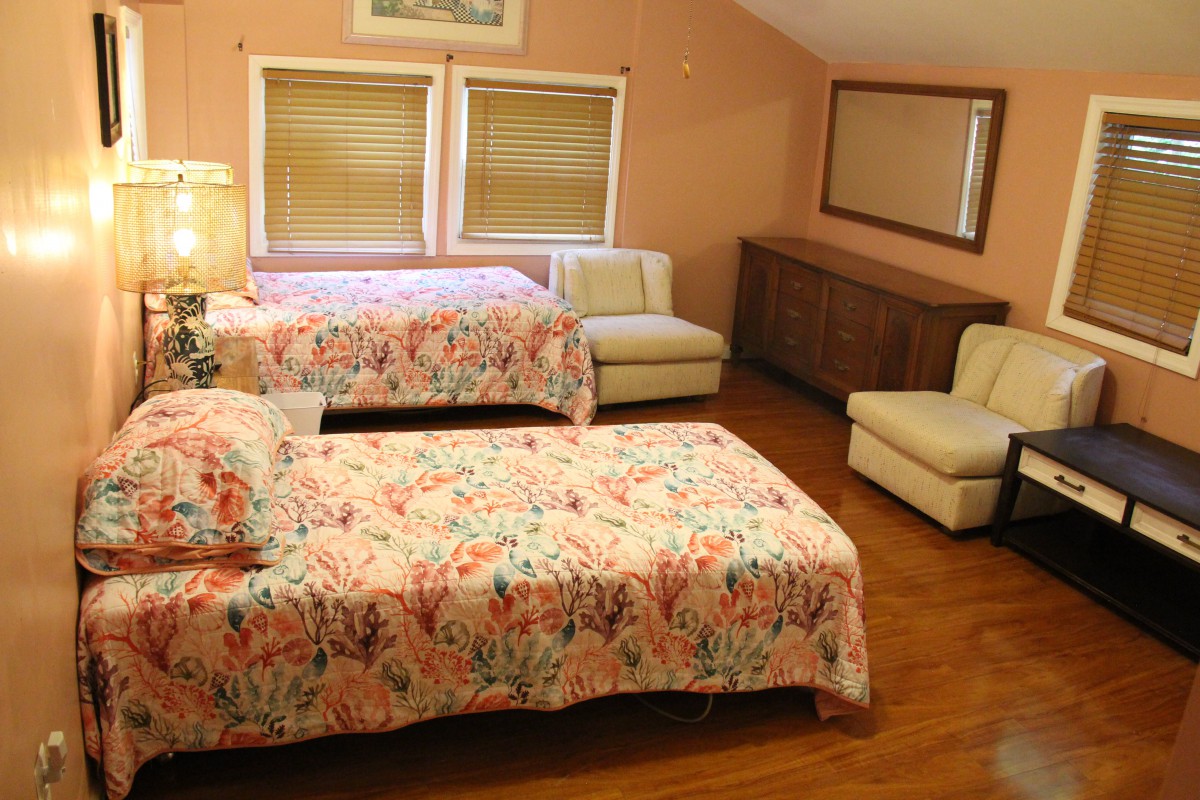 A cozy bedroom with two floral-covered beds, comfortable chairs, and wooden flooring.