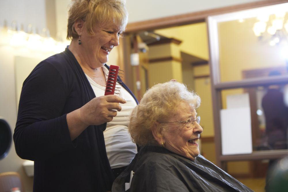 A hairdresser smiling while attending to an elderly woman at a salon.