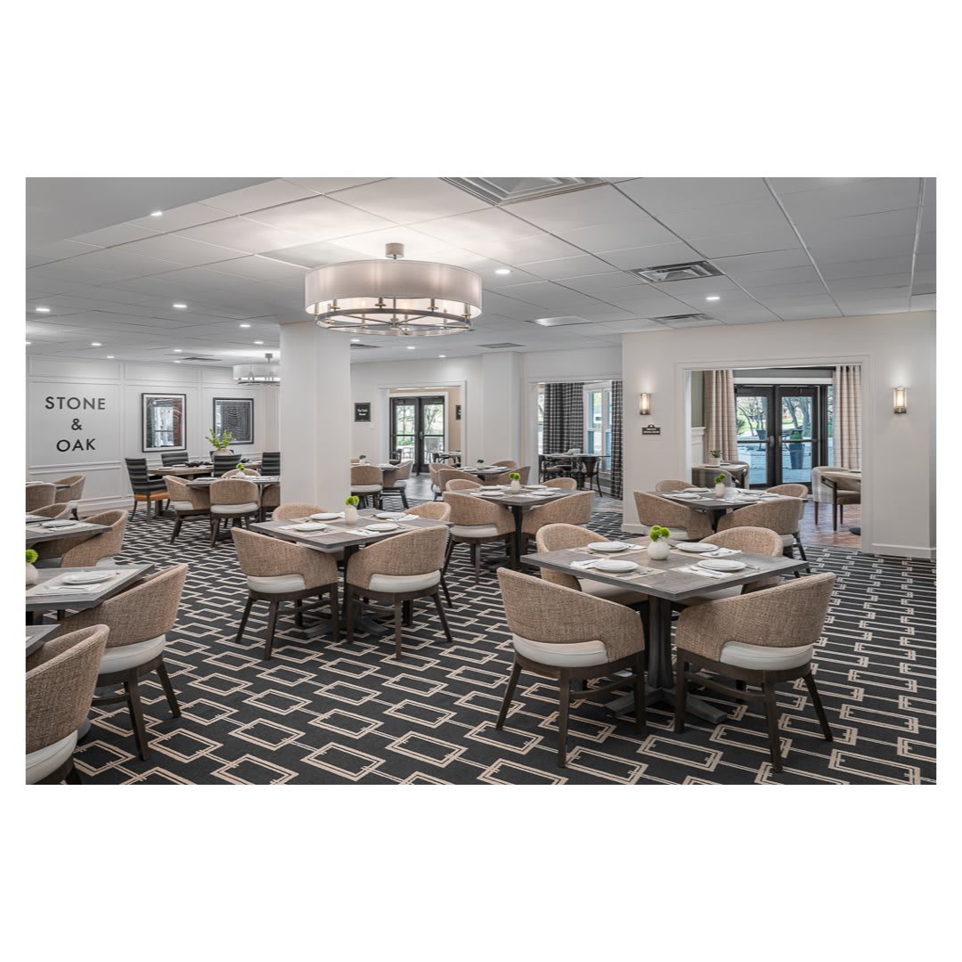 A modern dining room with neatly arranged tables and chairs, illuminated by a large chandelier.