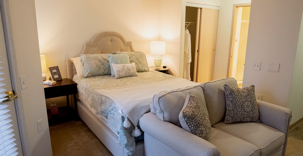 A cozy bedroom with a bed, sofa, and soft lighting.