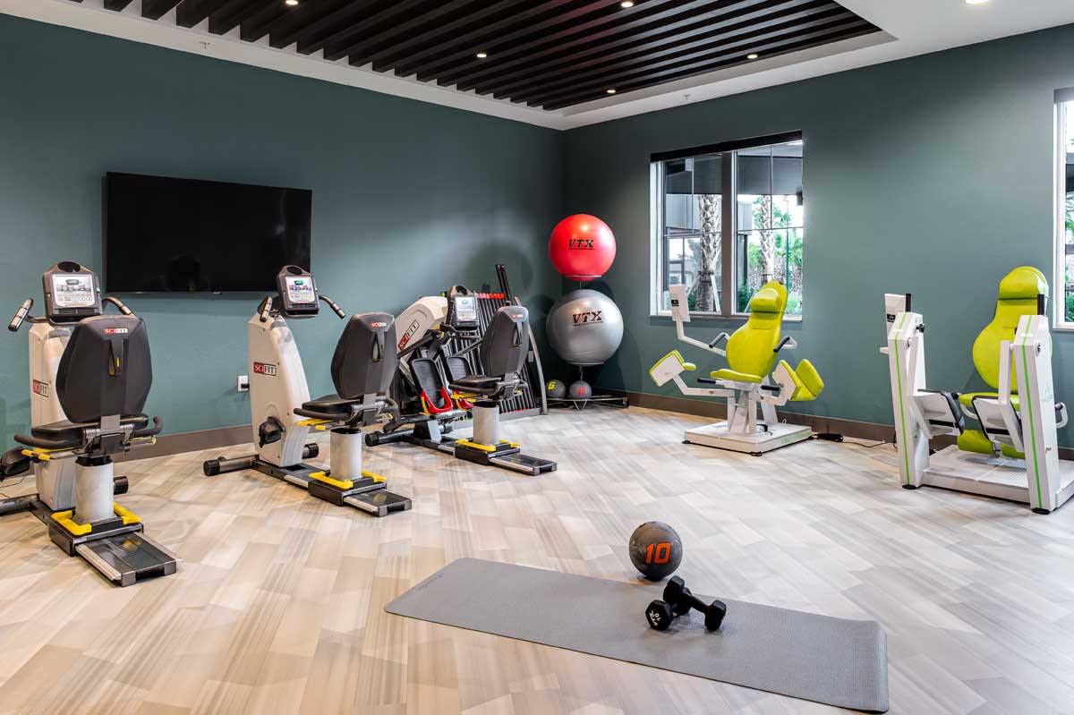 A modern gym with various exercise equipment, including cardio machines, weights, and a yoga mat.