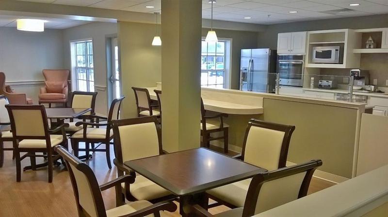 A modern dining area with wooden tables and chairs, adjacent to an open kitchen.