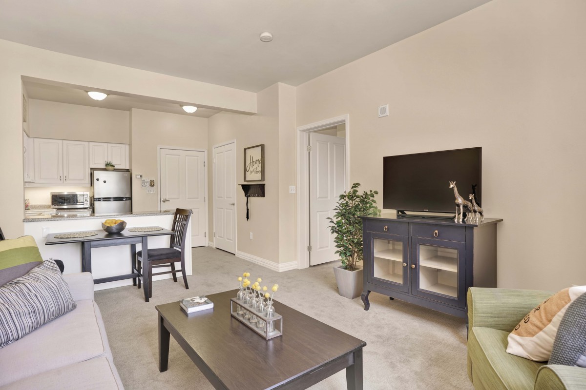 A modern living room with a view into the kitchen area, featuring a television, coffee table, and dining set.