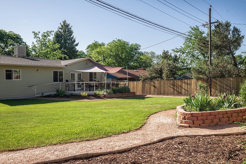 A well-maintained backyard with a green lawn, garden path, and a deck featuring a patio umbrella.