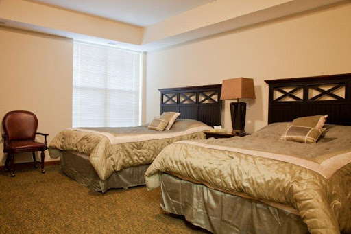 A cozy hotel bedroom featuring two twin beds with elegant bedding and a stylish lamp beside the window.