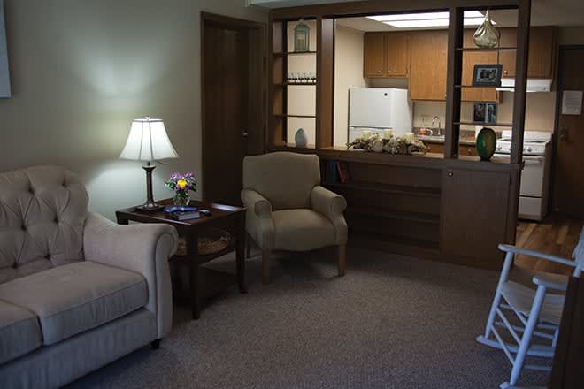 A cozy living room with a sofa, chair, and a view into the kitchenette.