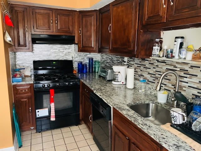 A kitchen interior with wooden cabinets, a granite countertop, and tiled backsplash.