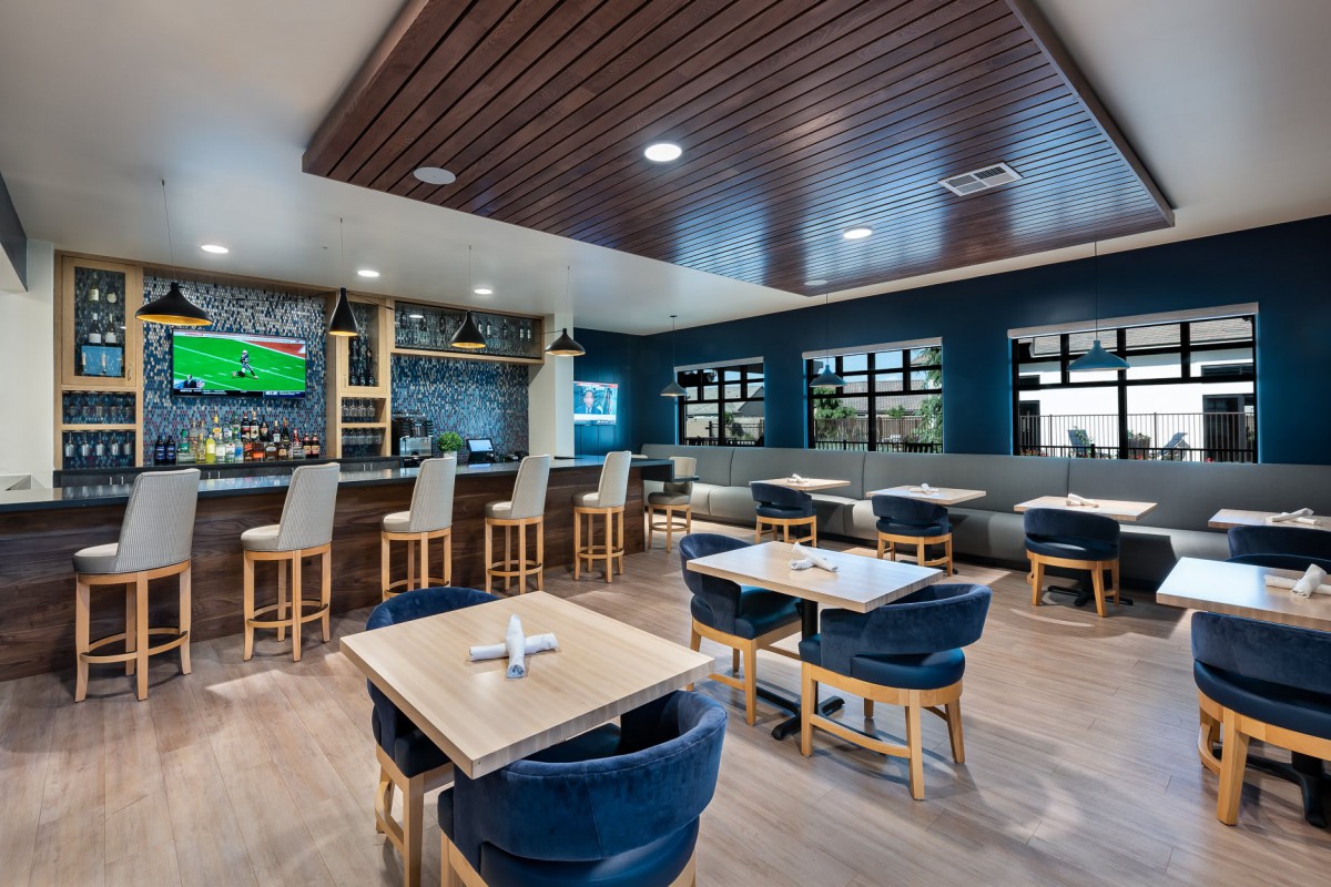 A modern restaurant interior with a bar area, featuring stylish seating and a wooden ceiling.