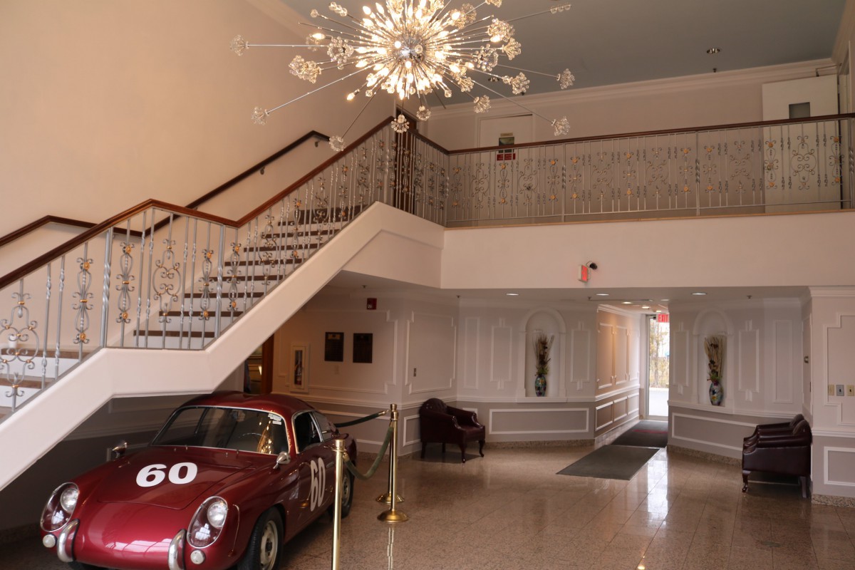 A classic car displayed in an elegant lobby with a staircase and chandelier.