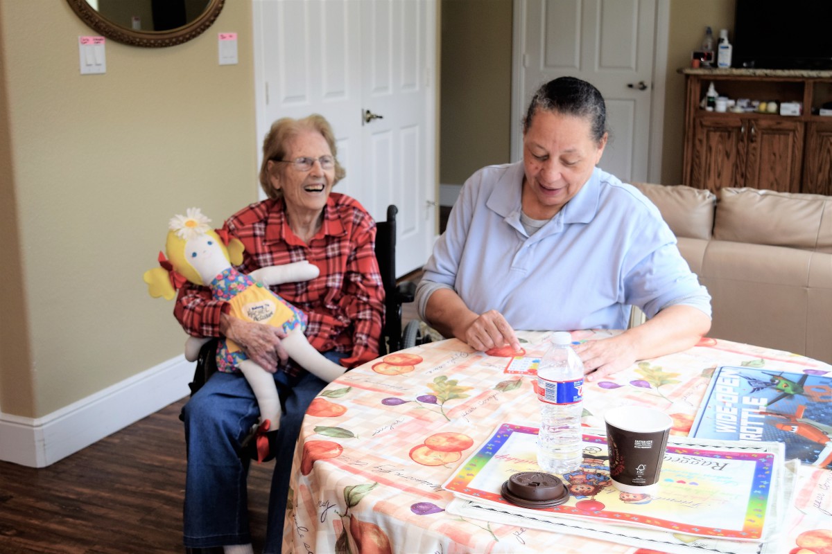 Two elderly individuals enjoying a moment together at a table, one holding a doll.