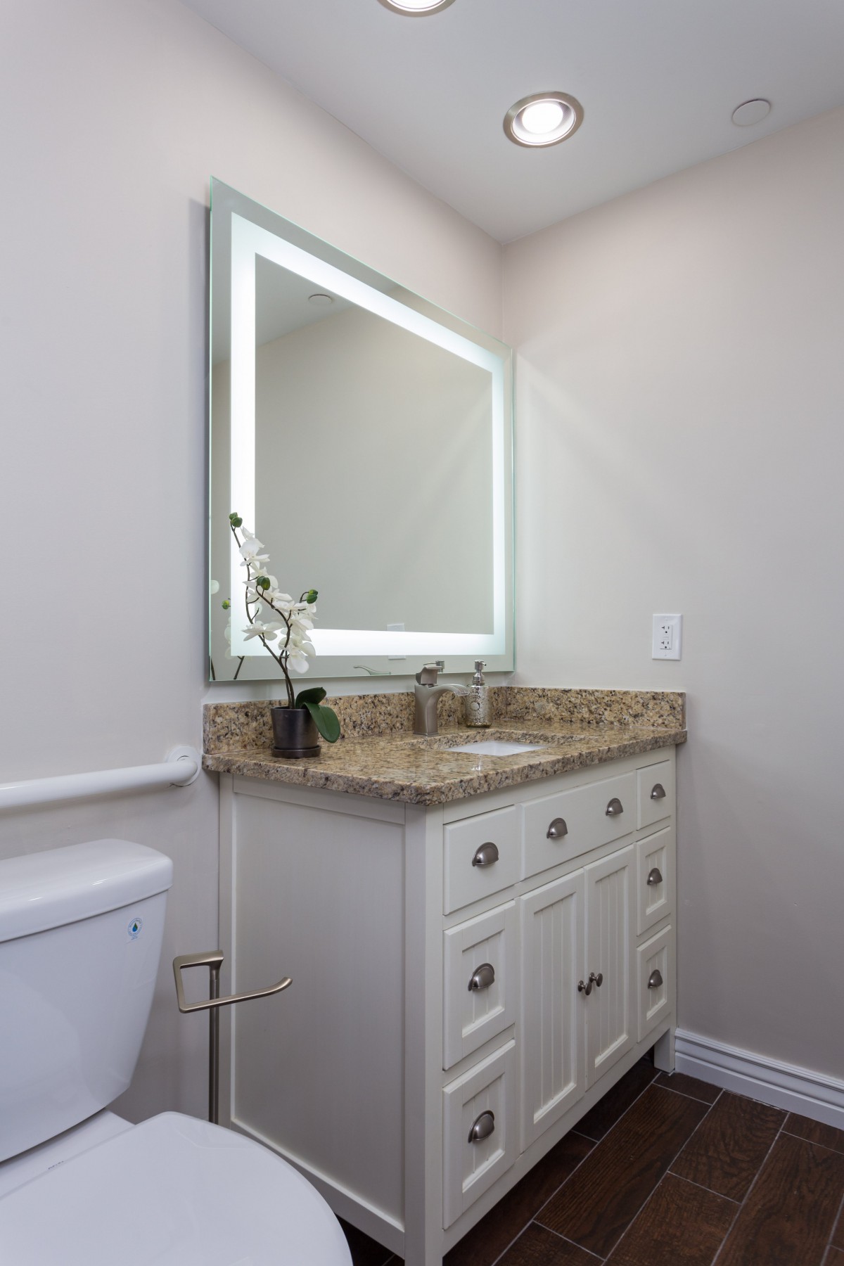 A modern bathroom with a granite countertop and illuminated mirror over the vanity.