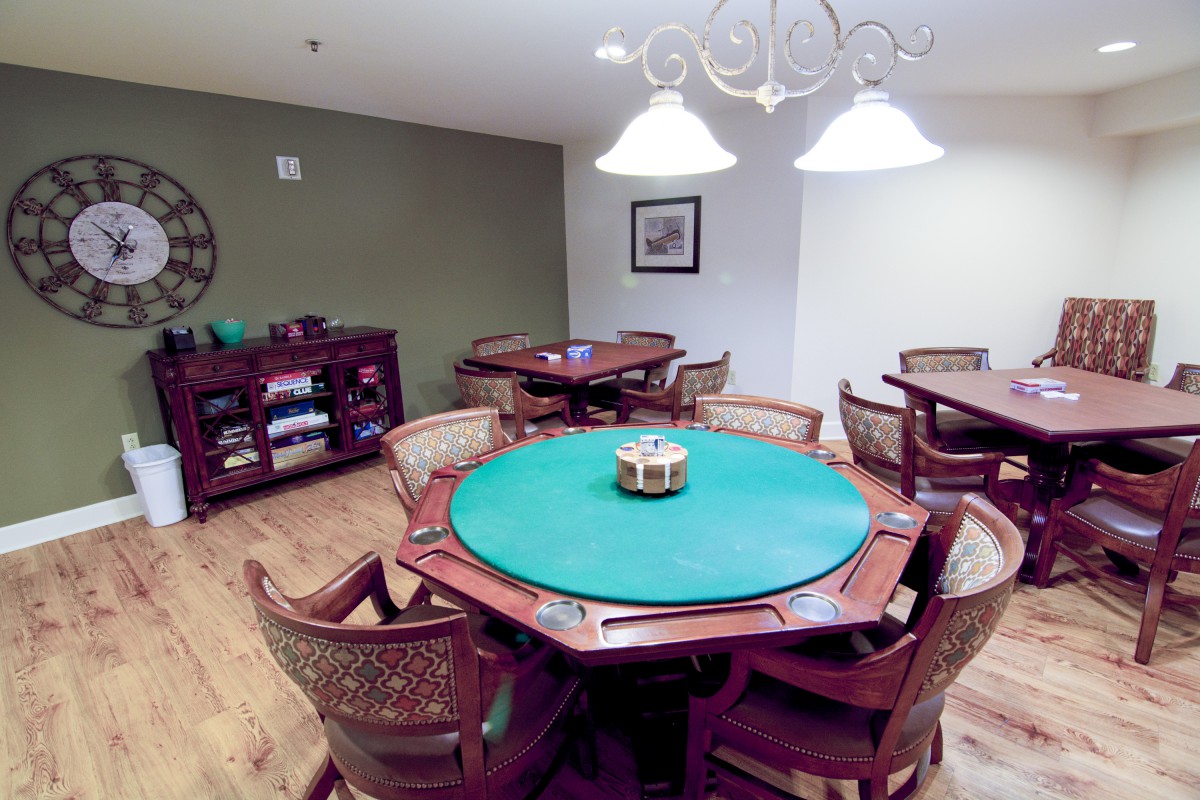 A cozy game room featuring a poker table surrounded by wicker chairs under warm lighting.