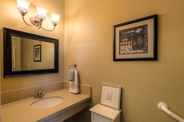 A well-lit bathroom featuring a sink, a mirror, and framed artwork on the wall.