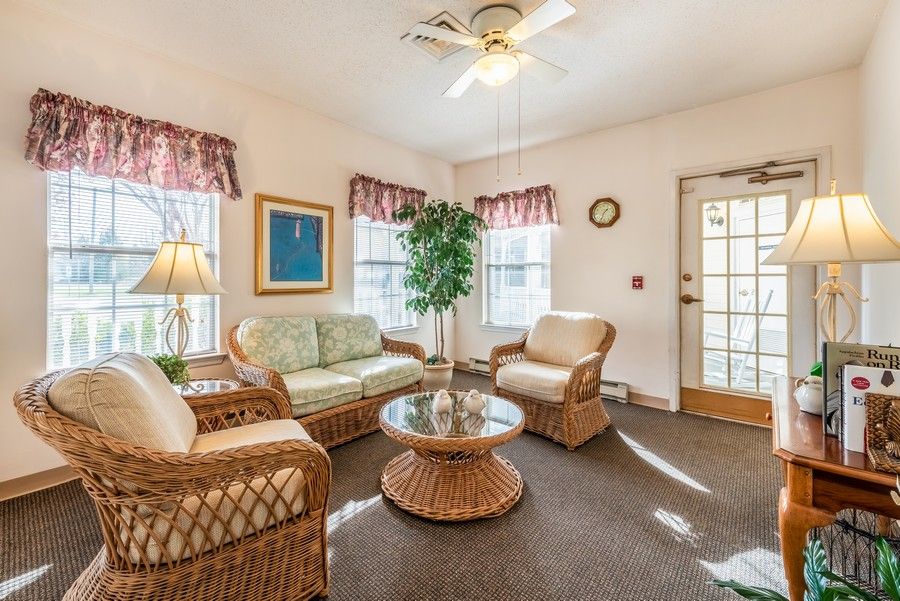 A cozy living room with wicker furniture and a coffee table, featuring large windows and an indoor plant.