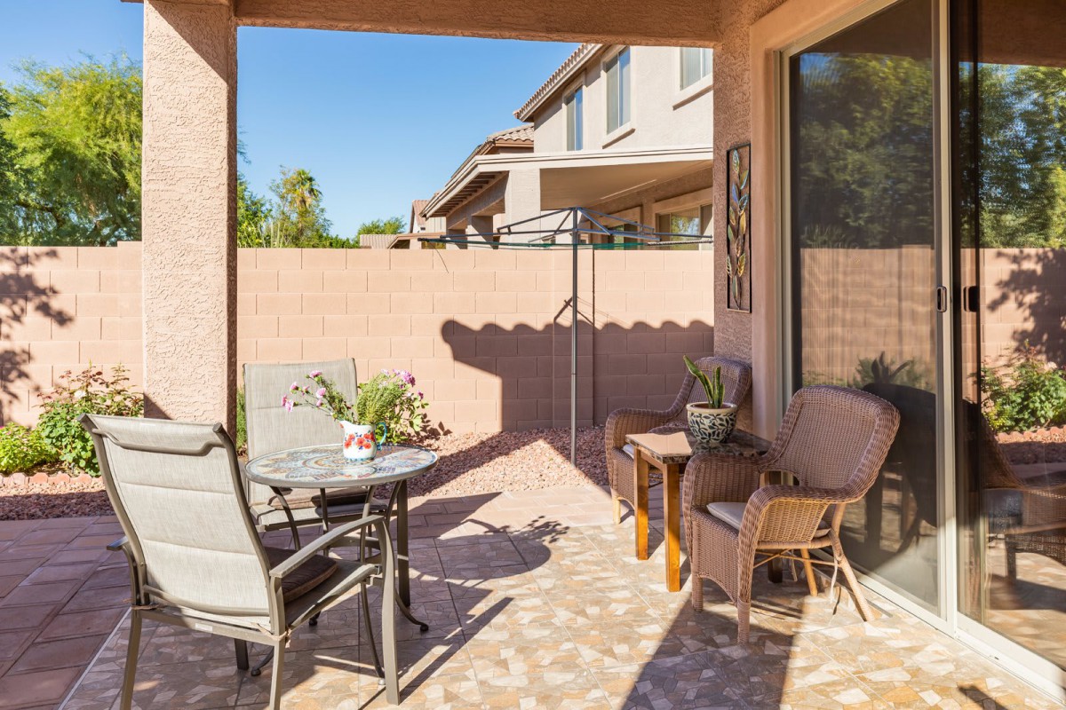 A sunny patio with comfortable outdoor seating, featuring a table and chairs, enclosed by a brick wall.