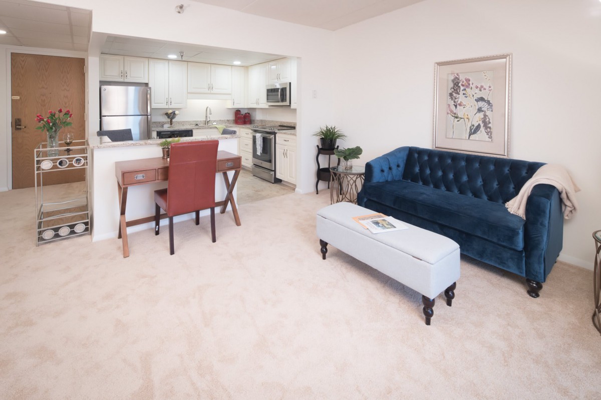 A modern open-space living room with a view into the kitchen, featuring a blue sofa and a small dining area.