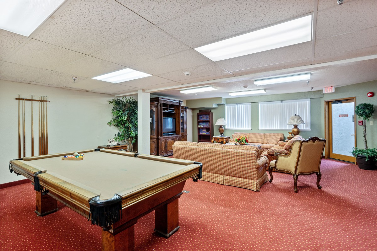 A cozy basement with a billiard table, sofa, and television setup.