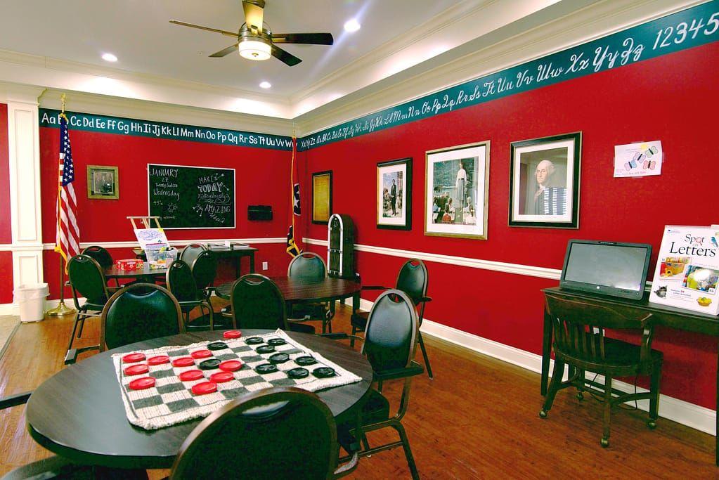 A cozy game room with red walls, featuring tables set up for checkers and decorated with artwork.