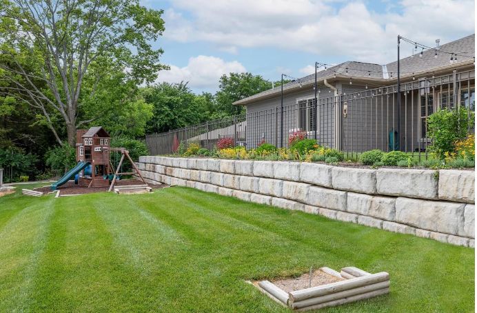 A backyard with a well-maintained lawn, retaining wall, and playground set.