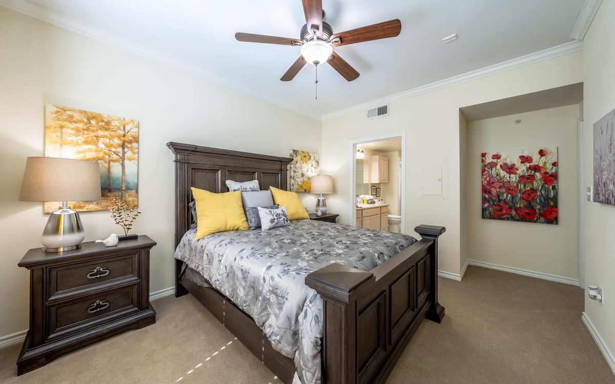 A cozy bedroom with a large wooden bed, decorative pillows, ceiling fan, and wall art.