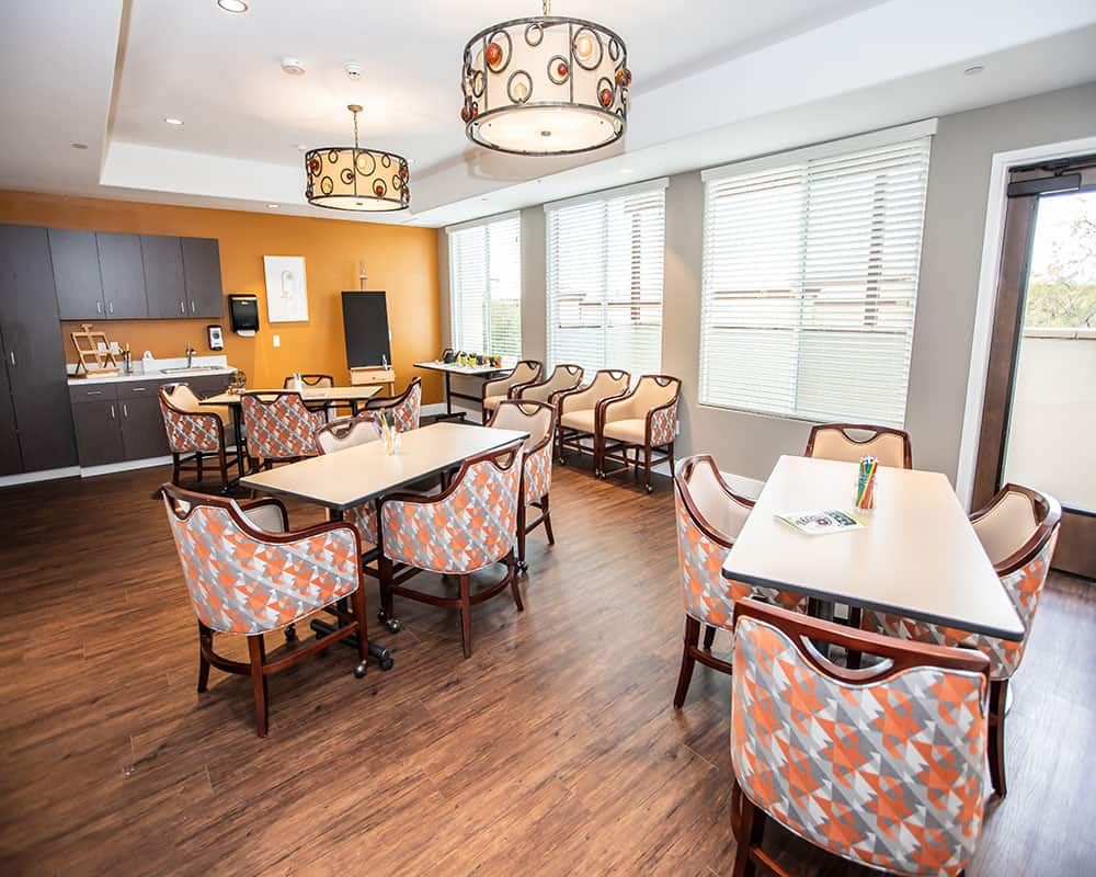 A modern dining area with tables and patterned chairs, featuring large windows and stylish lighting.