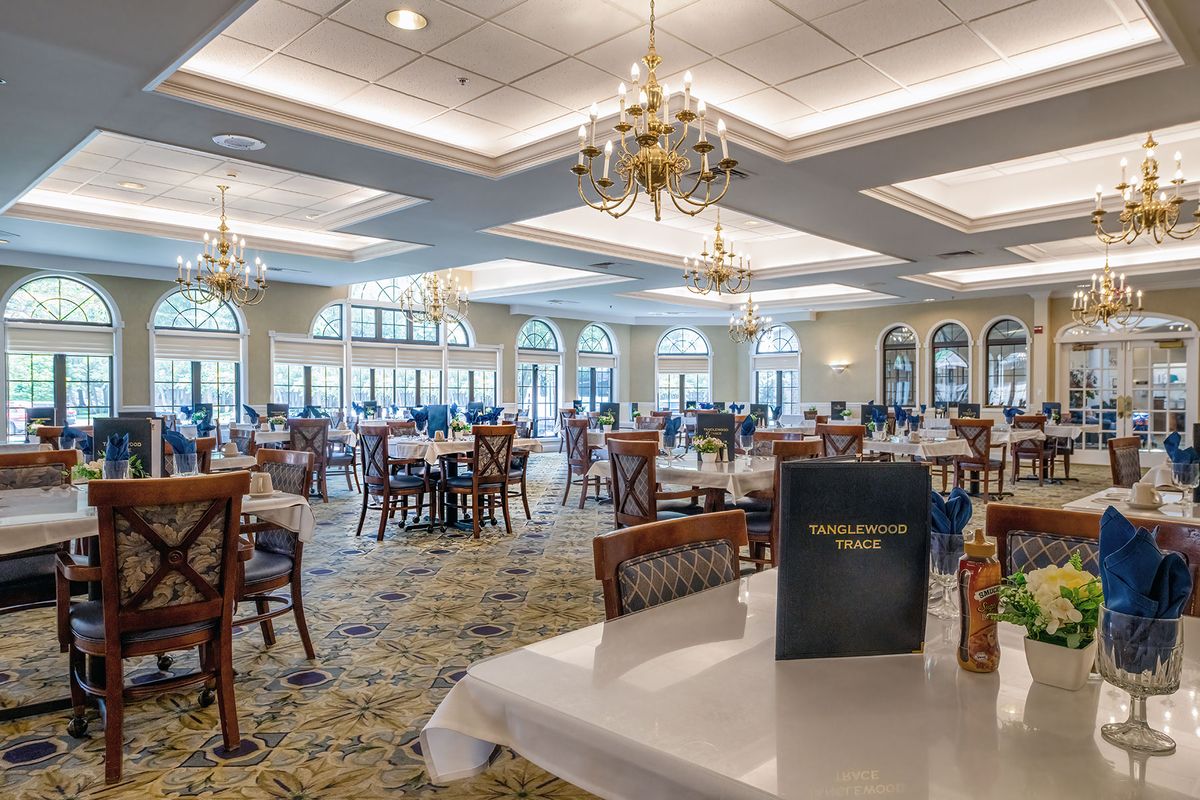 A spacious and elegantly decorated restaurant dining room featuring chandeliers and neatly arranged tables and chairs.