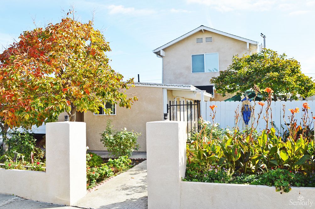 A residential house with a garden and trees in the front yard.