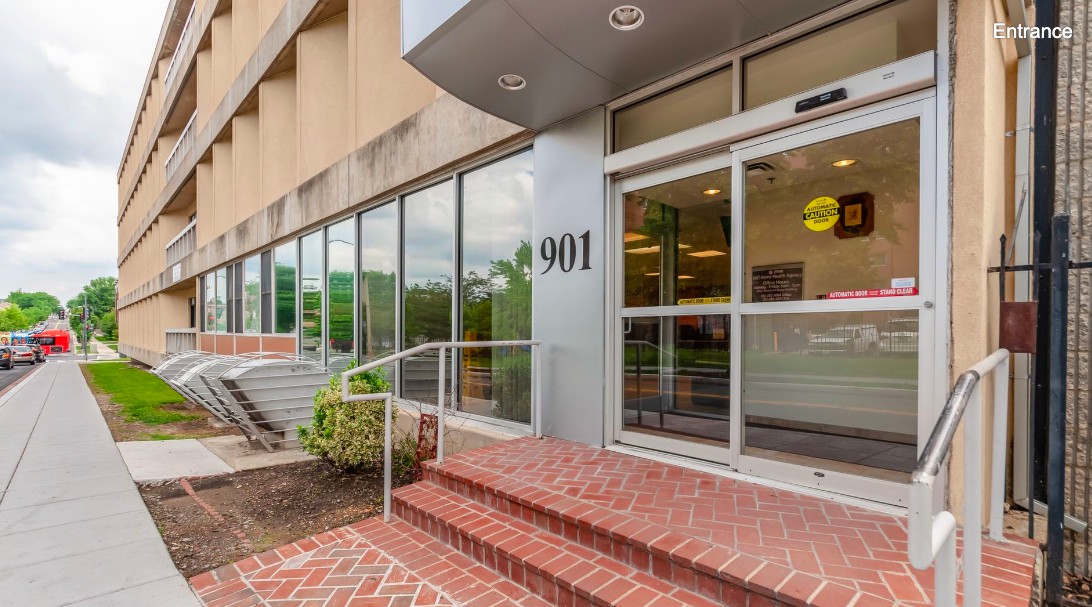 The entrance of an office building features brick steps leading to glass doors with the number 901 on the facade.