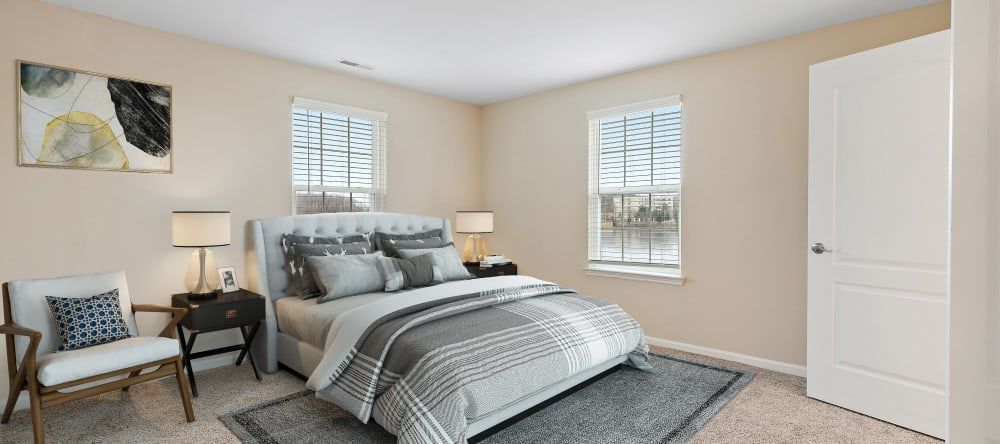 A modern, minimalist bedroom with gray and white bedding and natural light from two windows.