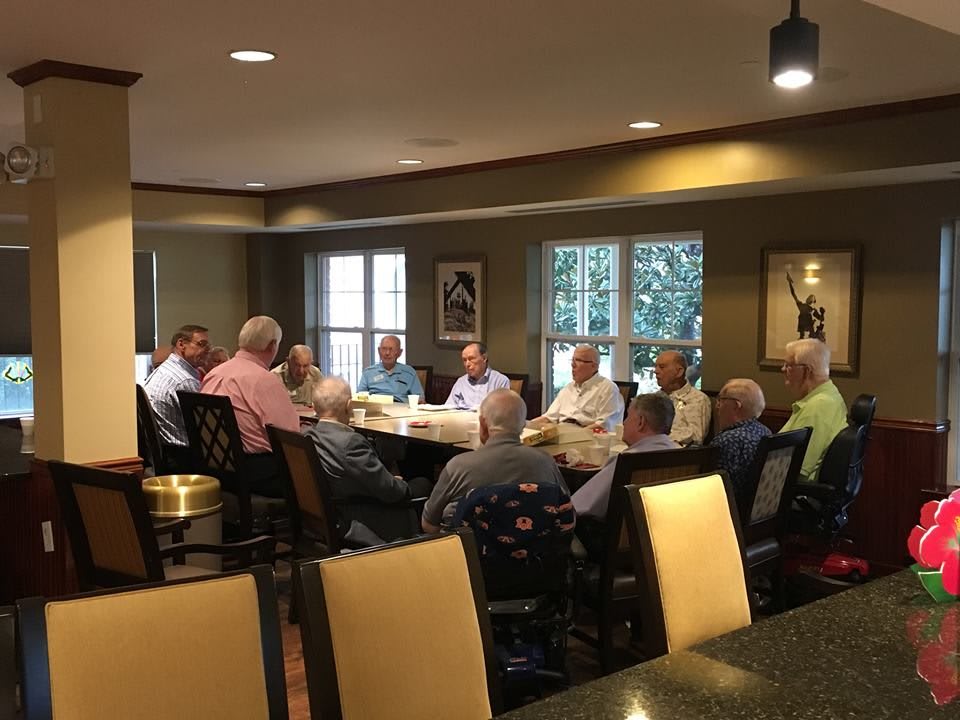 A group of seniors engaged in a meeting around a table in a well-lit room.