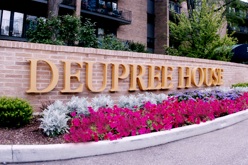 Entrance sign of Deupree House surrounded by colorful flowers.