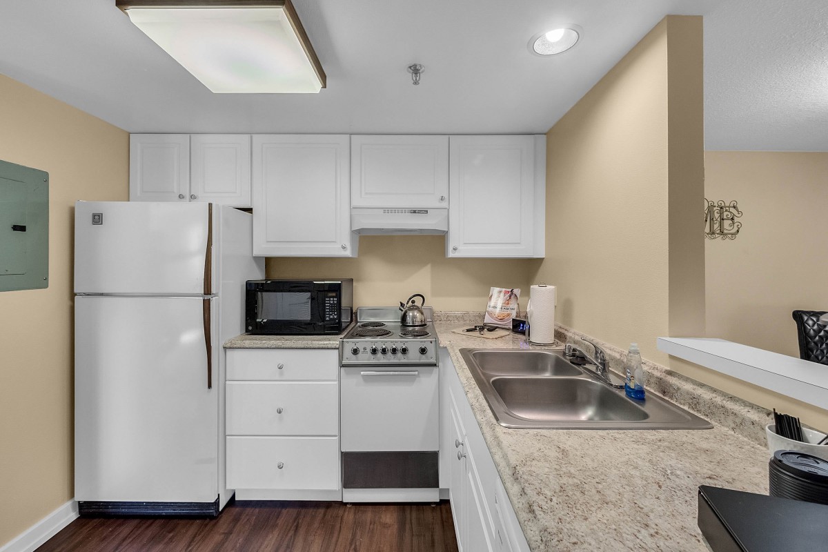 A modern kitchen with white cabinets and appliances, featuring a refrigerator, microwave, and stove.