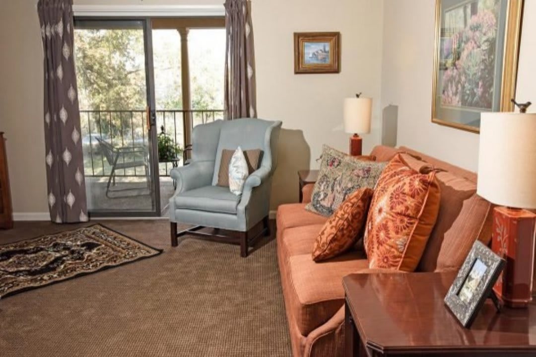 A cozy living room with a sofa, armchair, and decorative pillows near a sliding balcony door.