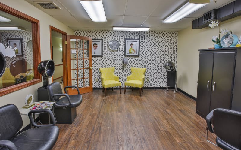 A cozy salon interior with yellow chairs, patterned wallpaper, and hair styling stations.