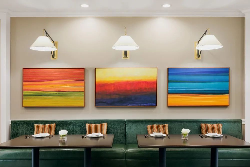 A modern restaurant dining area featuring abstract, colorful paintings and comfortable booth seating.
