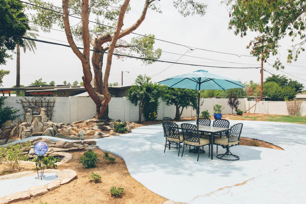 A serene backyard patio with a table, chairs, and umbrella set against a landscaped garden.