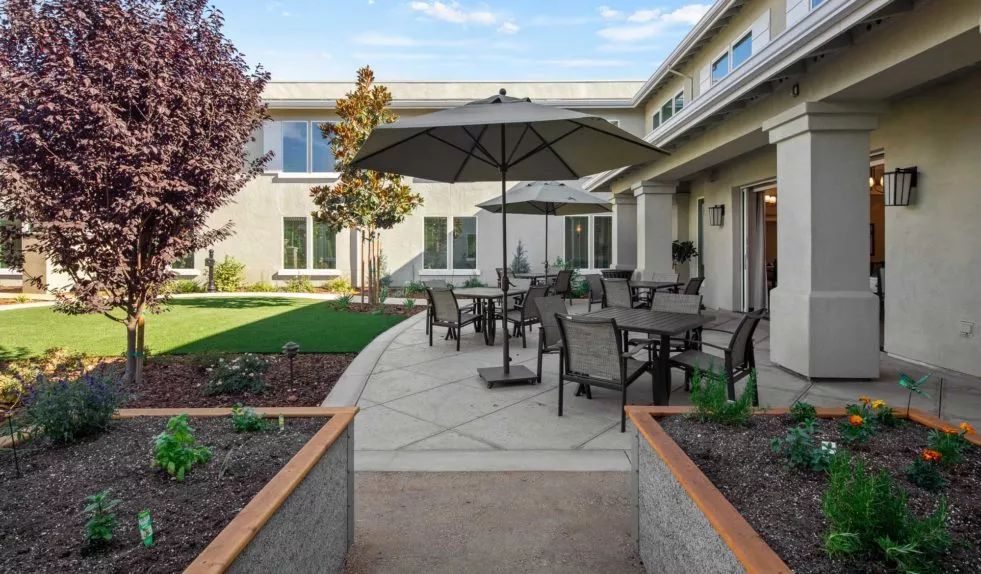 A well-maintained backyard patio featuring outdoor furniture and an umbrella, surrounded by a landscaped garden.