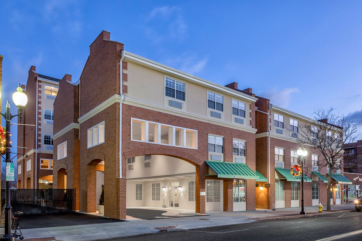 A modern residential building with brick and cream facade, seen at dusk from the street.